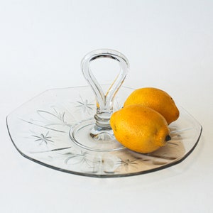 Könnte beinhalten: Ein transparentes Serviertablett aus Glas mit einem Griff, das mit einem Sternmuster verziert ist. Zwei gelbe Zitronen liegen auf dem Tablett.