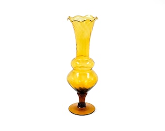 May include: A tall amber glass vase with a flared top and a bulbous body. The vase has a twisted stem and a wide, round base.
