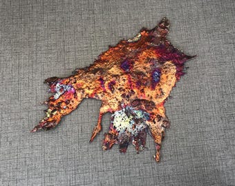 May include: A large, abstract, metallic sculpture with a unique, organic shape. The sculpture is made of copper and has a variety of colors, including red, orange, yellow, green, blue, and purple. The sculpture is textured and has a rough, uneven surface.