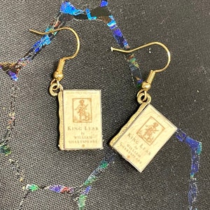 Puede incluir: Pendientes de oro con un dije de libro en miniatura con el texto "King Lear by William Shakespeare".