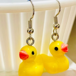 May include: A pair of yellow rubber ducky earrings with silver hooks. The ducks have black eyes and red beaks.