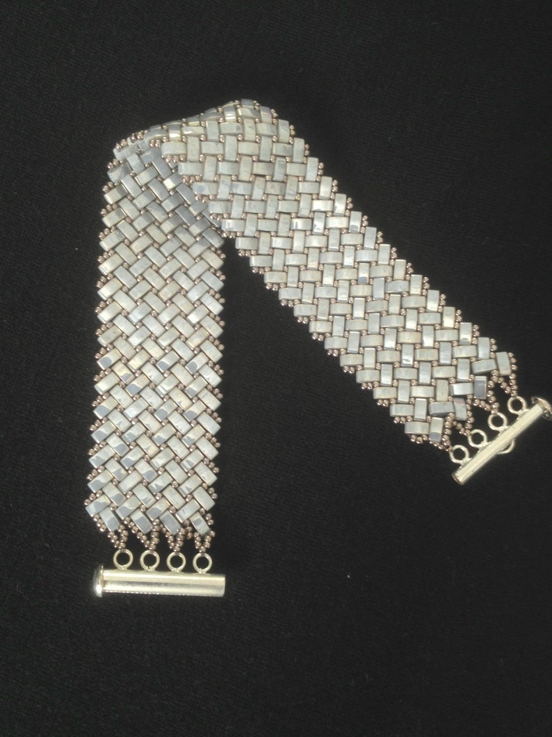 May include: A silver bracelet with a woven design made of small, iridescent white beads. The bracelet has a silver clasp.