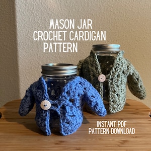 Op de afbeelding: Twee glazen potten met gebreide vesten. De vesten zijn blauw en groen. De tekst "MASON JAR CROCHET CARDIGAN PATTERN INSTANT PDF PATTERN DOWNLOAD" staat op de tafel onder de potten.