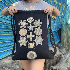 Może przedstawiać: Czarny plecak ze sznurkiem i kolorowym geometrycznym wzorem. Torba ma czarne paski ze sznurka i metalowe przelotki. Geometryczny wzór zawiera różne kształty i kolory, takie jak żółty, pomarańczowy i niebieski, tworząc żywy design.