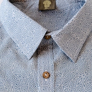 May include: A blue and white patterned button-up shirt with a collar and two buttons. The shirt has a geometric pattern and the label says "XL".