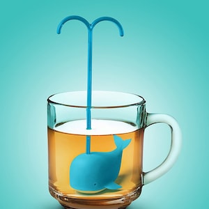 May include: A blue whale-shaped tea infuser with a blue handle sits in a clear glass mug filled with tea.