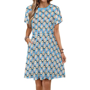 May include: A light blue, short-sleeved dress featuring a repeating pattern of stylized faces. The faces have black hair, a mustache, and a red stripe. The dress has pockets and a round neckline.