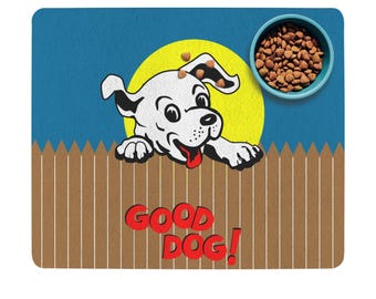 May include: A dog-themed placemat with a cartoon dog peeking over a wooden fence. The dog is white with a red tongue, set against a yellow circle and blue background. The words "GOOD DOG!" are in red. A blue bowl of dog food is in the upper right.