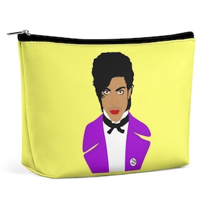 Puede incluir: Una bolsa amarilla con cremallera con una ilustración de Prince en morado y blanco, con un traje morado y una pajarita blanca. La ilustración incluye el texto "Purple Boy".