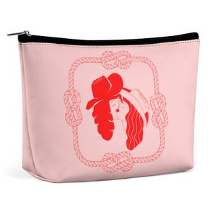 May include: A pale pink cosmetic bag with a black zip. The bag features a red illustration of two figures kissing, framed by a rope design. The illustration is in the centre of the bag.