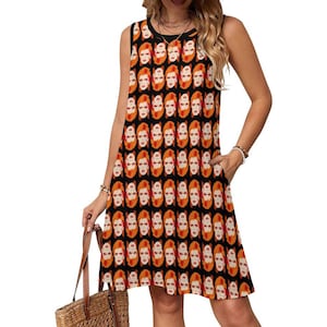 Könnte beinhalten: Ärmelloses schwarzes Kleid mit einem sich wiederholenden Muster aus orangefarbenen und weißen Gesichtern. Das Kleid hat einen schwarzen Ausschnitt und Armausschnitte. Das Model hält eine braune Korbtasche. Das Kleid ist knielang und hat Taschen.