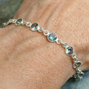 May include: A silver-toned chain bracelet featuring a series of round, bezel-set iridescent stones. Each stone displays a multi-colored, rainbow-like sheen. The links are connected by small silver-toned metal loops, creating a continuous, flexible band.