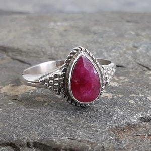 May include: A silver ring with a teardrop-shaped ruby gemstone set in a decorative silver setting.