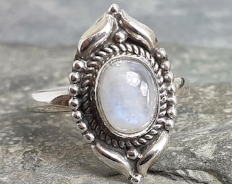 May include: A silver ring featuring a moonstone set in an intricate ornate design.