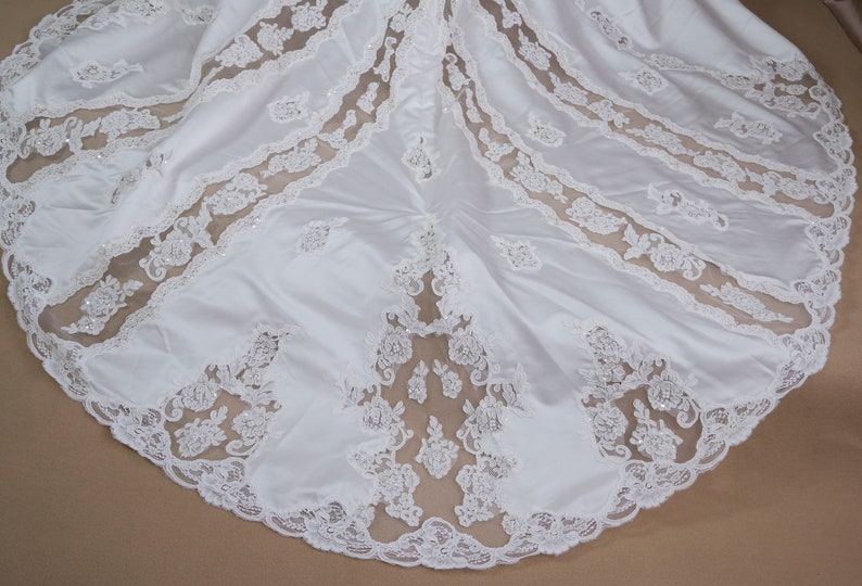 May include: White satin wedding dress with a lace overlay. The lace is a delicate floral pattern with a scalloped edge.