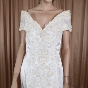 Puede incluir: Un vestido de novia de satén blanco con escote de corazón y tirantes de hombros descubiertos. El vestido está adornado con delicados abalorios y encaje.