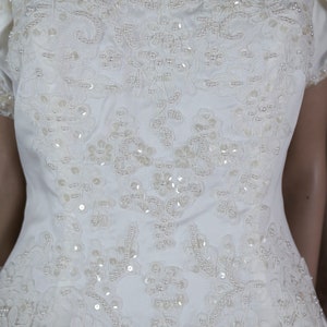 May include: A white satin wedding dress with a lace bodice and pearl embellishments. The dress has a sweetheart neckline and short sleeves.
