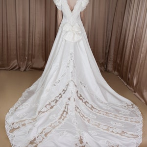 May include: A white satin wedding dress with a lace overlay and a large bow at the back.