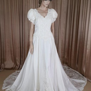 May include: A white satin wedding dress with a lace trim and a sweetheart neckline. The dress has puffed sleeves and a long train.