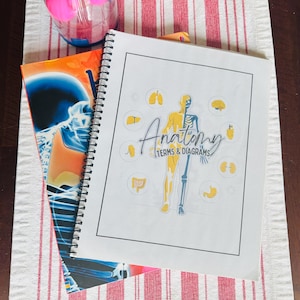May include: Two spiral-bound anatomy books on a red and white striped surface. The top book has the title "Anatomy Terms & Diagrams" with a diagram of a human figure. The other book has a blue and orange cover with a skeleton image.