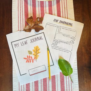 May include: A leaf journal and leaf journaling worksheet with a pencil and leaves on a red and white striped cloth. The journal has the text "MY LEAF JOURNAL" and a space for a name. The worksheet has prompts for leaf observation.
