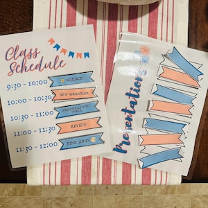 May include: Two laminated sheets featuring a class schedule and presentation labels. The schedule lists times from 9:30 to 12:00 with blue and peach banner icons for subjects like Science, New Grammar, Presentation/Snack, Review, and Fine Arts.