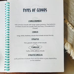 May include: A spiral-bound notebook open to a page titled "TYPES OF CLOUDS." The page lists and describes different cloud formations, including Cumulonimbus, Cirrus, Stratus, Cumulus, and Stratocumulus. The notebook has a teal spiral binding.