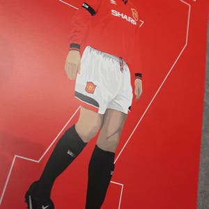 May include: Illustration of a soccer player in a red jersey with white shorts and black socks. The jersey has the word "SHARP" and the number "7" on it. The background is red with white lines and the name "CANTONA".