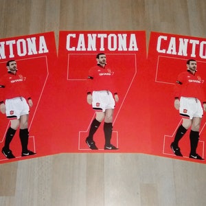 May include: Three red posters featuring a soccer player in a red jersey with the name "CANTONA" above and the number "7" on the jersey. The player is wearing white shorts and black socks and shoes.
