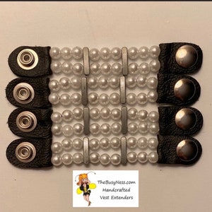May include: Four black leather vest extenders with pearl and silver accents. Each extender has a button and loop closure. The extenders are handmade and are available on TheBusyNess.com.