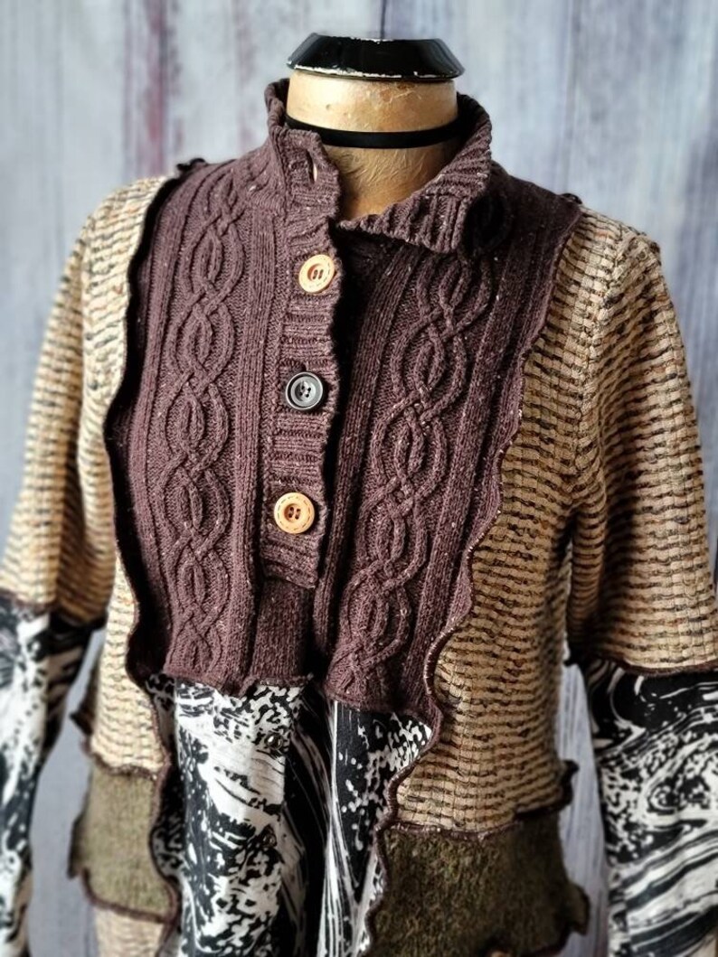 May include: A brown and tan patchwork sweater with a cable-knit collar and button closure. The sweater features a mix of textures and patterns, including a patterned sleeve and a decorative trim.