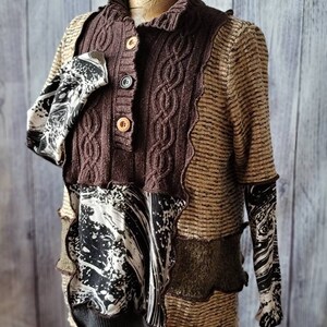 May include: A unique, patchwork-style sweater with a brown cable-knit front and collar, accented by tan and patterned fabric panels. The sweater features button closures and a mix of textures, creating a layered look. The sleeves have a black and white pattern.