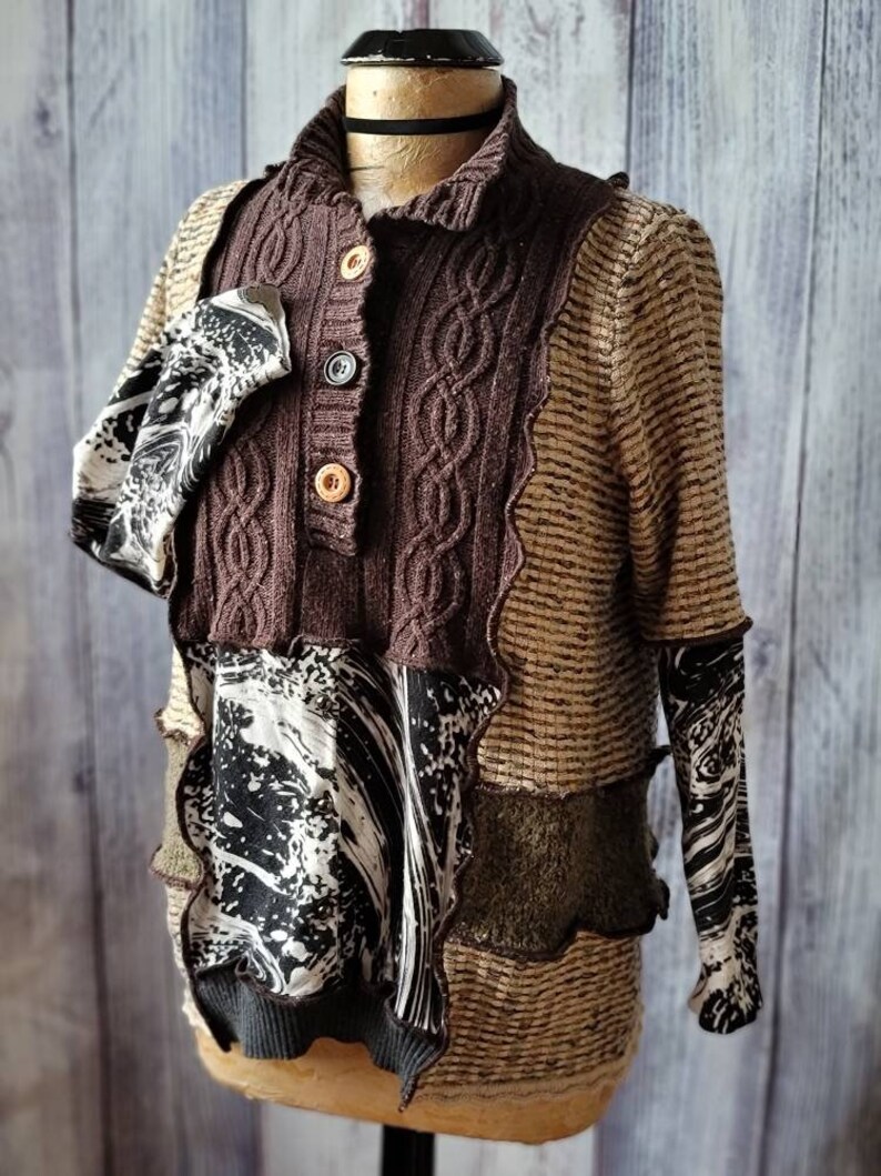 May include: A unique, patchwork-style sweater with a brown cable-knit front and collar, accented by tan and patterned fabric panels. The sweater features button closures and a mix of textures, creating a layered look. The sleeves have a black and white pattern.