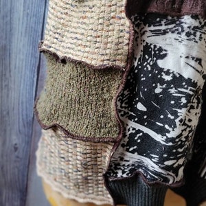 May include: A patchwork garment featuring a mix of textures and patterns. The design incorporates woven, knit, and printed fabrics in neutral tones with accents of black and brown. The garment has a ribbed cuff and a layered construction.