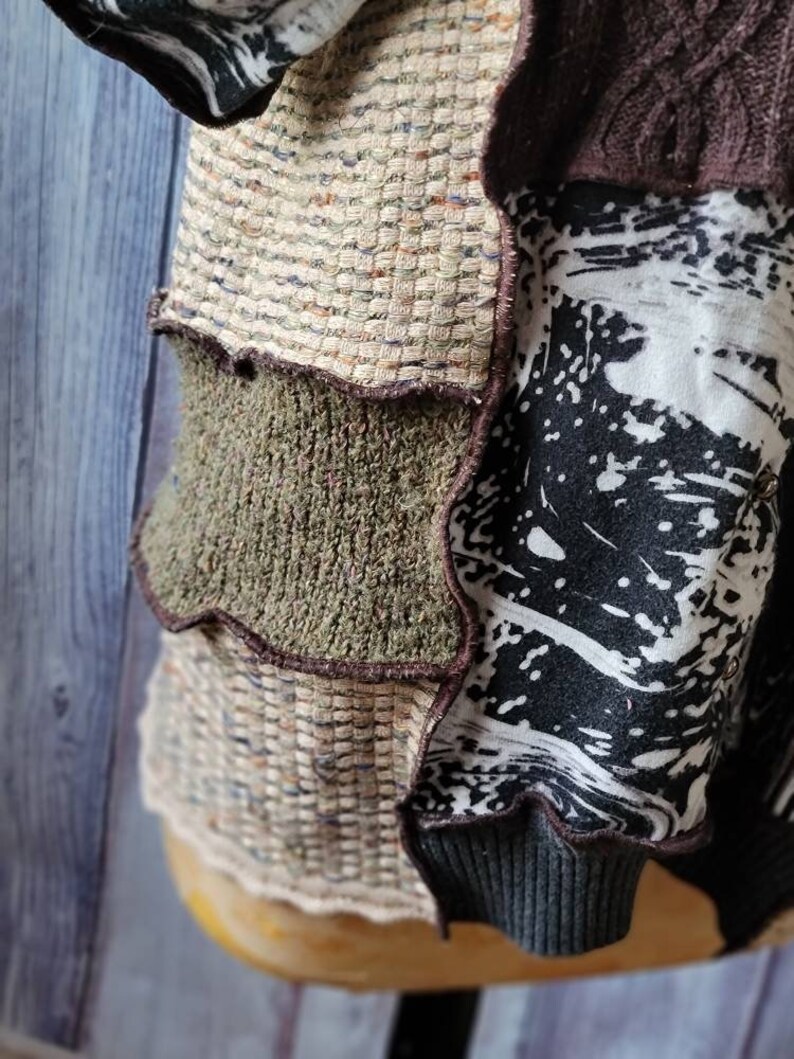 May include: A patchwork garment featuring a mix of textures and patterns. The design incorporates woven, knit, and printed fabrics in neutral tones with accents of black and brown. The garment has a ribbed cuff and a layered construction.