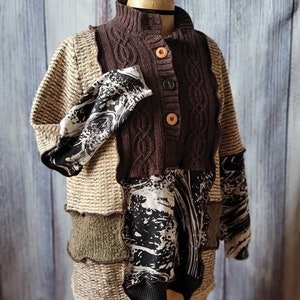 May include: A patchwork sweater displayed on a mannequin. The sweater features a brown cable-knit bodice with wooden buttons, tan sleeves, and panels of olive green and black and white patterned fabric. The sweater has a high collar.
