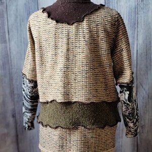 May include: A textured sweater with a brown turtleneck and sleeves with a black and white pattern. The body of the sweater is beige with brown and black flecks, and a green band across the midsection. The bottom edge has a scalloped trim.