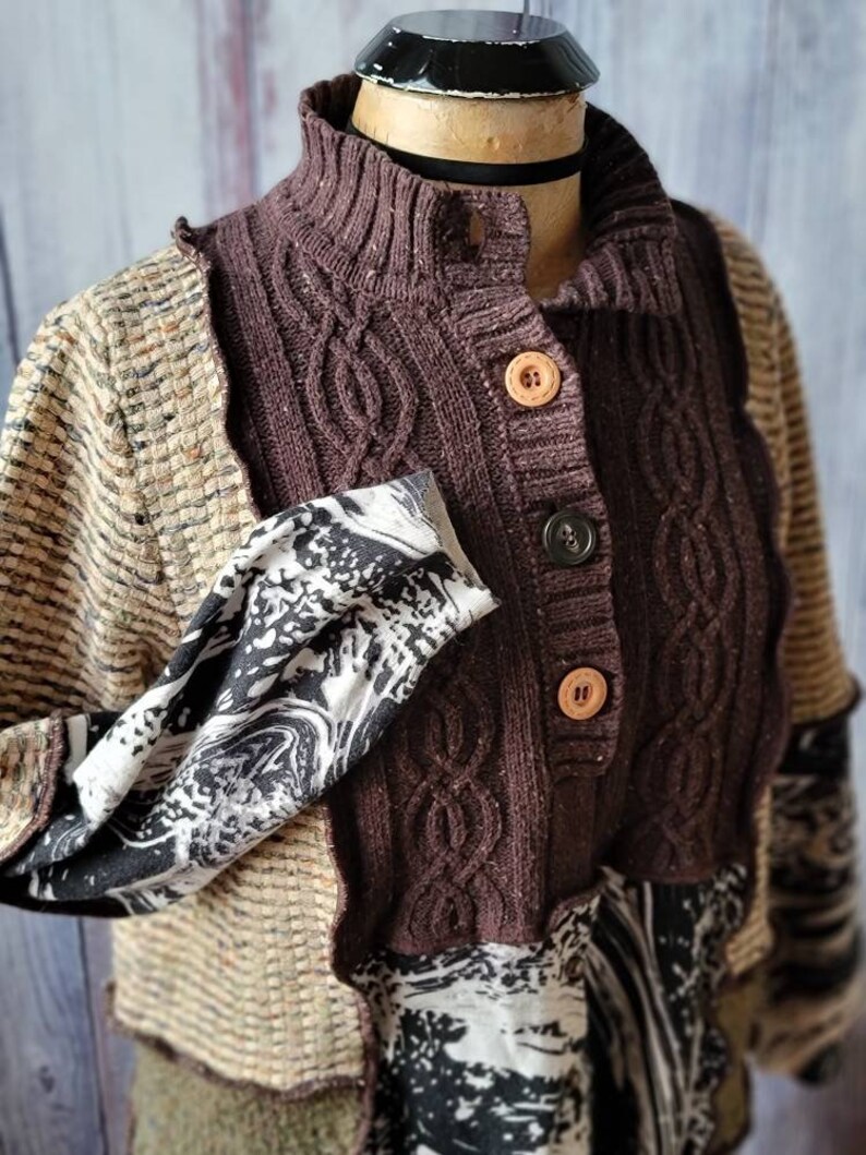 May include: A patchwork cardigan with a high collar and wooden buttons. The sweater features a mix of textures and patterns, including cable knit, woven fabric, and a black and white print. The color palette includes shades of brown, beige, and black.