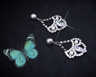 May include: A pair of silver dangle earrings with clear crystal accents. The earrings have a teardrop shape and are adorned with multiple small crystals.