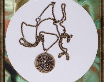 May include: A gold-toned necklace with a round pendant featuring a circular design with concentric circles and a small dot in the center.