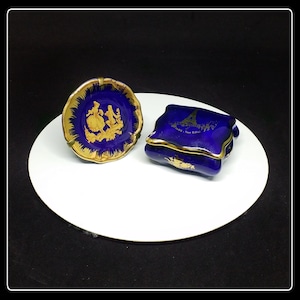 May include: Two small blue and gold porcelain trinket boxes. One box features a gold design of a couple dancing, the other box features a gold design of the Eiffel Tower with the text "Paris - Tour Eiffel".