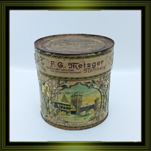 May include: Vintage tin container with a colourful illustration of a building and a bridge. The text on the tin reads "F.G. Hetzger. Kol. Bayer. Hof-Lebkuchen- und Chocolade-Fabrikant. Turnberg."