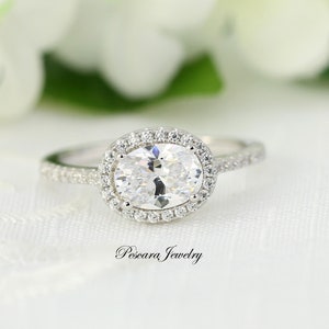 May include: A silver ring with a large oval-shaped clear stone surrounded by a halo of smaller clear stones. The ring has a band of smaller clear stones.