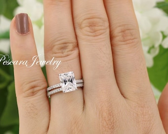 May include: A silver ring set with a large, square-shaped, clear gemstone. The ring is worn on the ring finger of a hand with a light brown nail polish.