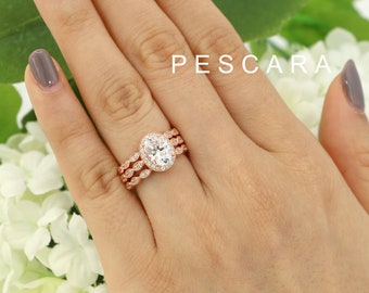May include: A three-piece rose gold engagement ring set with an oval-shaped center stone and a halo of smaller stones. The band is adorned with delicate, twisted details.