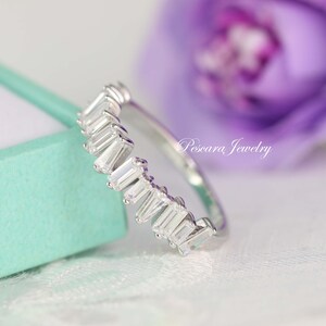 May include: A silver ring with a row of baguette-shaped clear stones. The ring is on a light blue background.