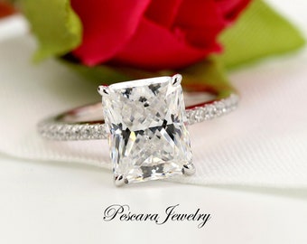 May include: A silver ring with a large, square-shaped, clear diamond. The diamond is set in a prong setting and the band is accented with smaller diamonds.