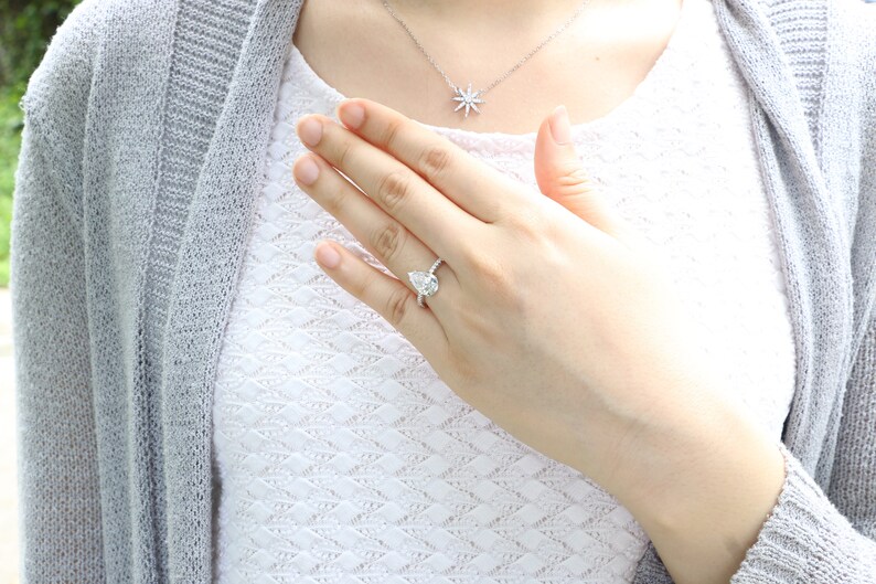 May include: A pear-shaped diamond engagement ring with a halo of smaller diamonds set in a white gold band.