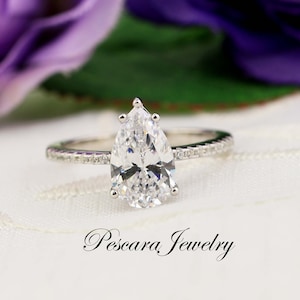 May include: A pear-shaped diamond engagement ring with a pave band. The ring is set in silver and features a large, clear diamond.