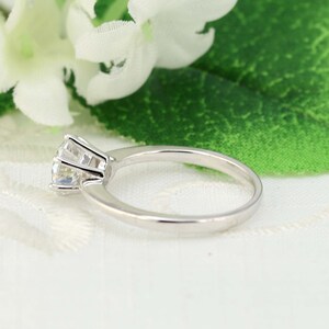 May include: A silver ring with a single, round, clear gemstone set in a prong setting.